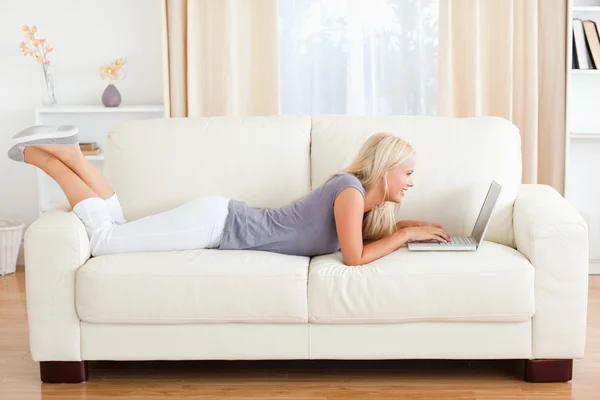 Kobieta, leżąc na kanapie przy pomocy pewien laptop — Zdjęcie stockowe