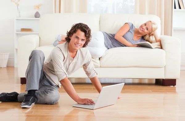 Man med en bärbar dator medan hans flickvän är med en bok — Stockfoto