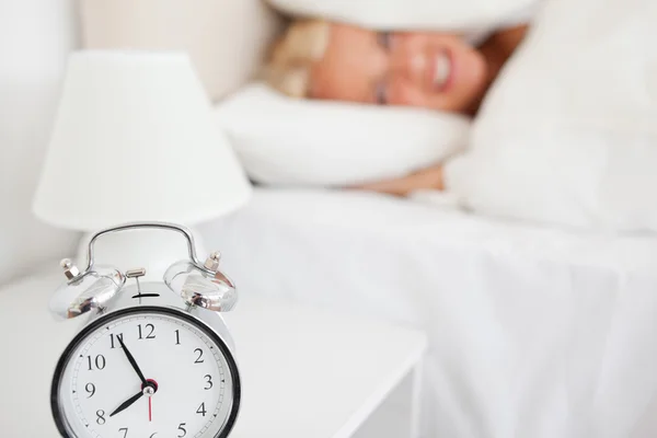 Mujer escondiendo su cabeza en una almohada mientras el despertador es el anillo — Foto de Stock