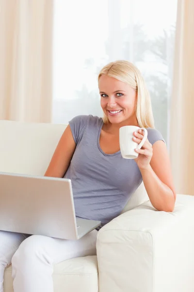 Retrato de uma mulher tomando um chá enquanto segura um laptop — Fotografia de Stock
