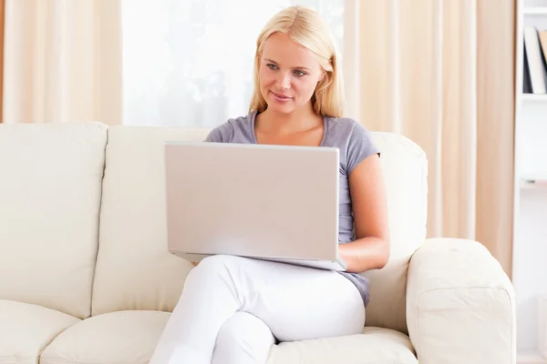 Bir dizüstü bilgisayar kullanırken kanepede oturan kadın — Stok fotoğraf
