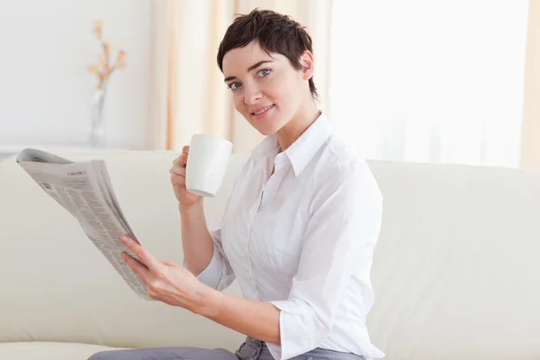 Frau mit einer Tasse, die Nachrichten liest, während sie in die Kamera schaut — Stockfoto