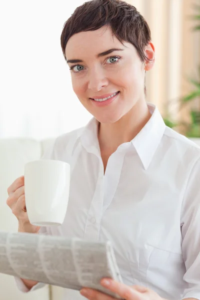 Encantadora mujer con una taza y un periódico — Foto de Stock