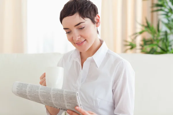 Brunette vrouw met een kop en een krant — Stockfoto