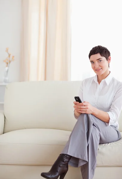 Uroczy kobieta siedzi na kanapie z telefonem — Zdjęcie stockowe