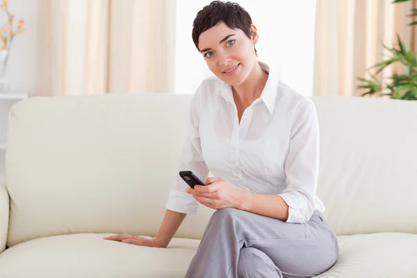 Leende brunett kvinna sitter på en soffa med en telefon — Stockfoto