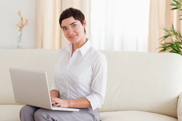 Bir dizüstü bilgisayar ile bir kanepede oturan kadın — Stok fotoğraf