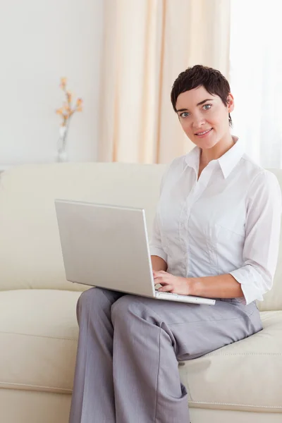 Bir dizüstü bilgisayar ile bir kanepede oturan sevimli kadın — Stok fotoğraf