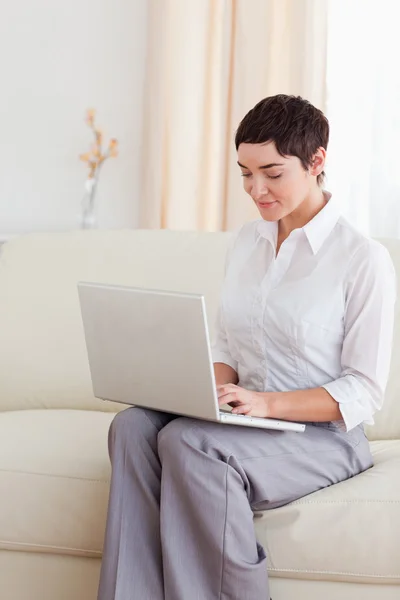 Uroczy kobieta siedzi na kanapie z laptopem — Zdjęcie stockowe