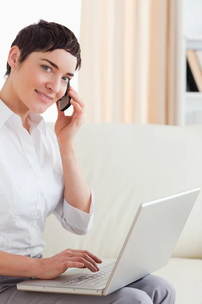 Short-haired woman with a laptop and a phone looking into the ca — Stock Photo, Image