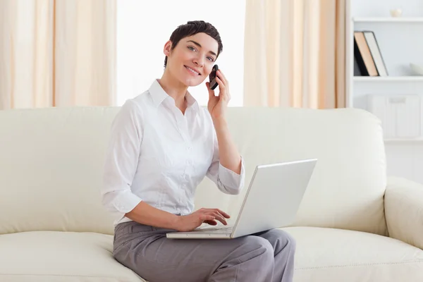Gorgeous woman with a laptop and a phone looking into the camera — Stock Photo, Image