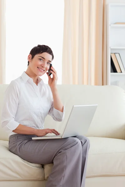 Cute Woman with a laptop and a phone looking into the camera — Stock Photo, Image