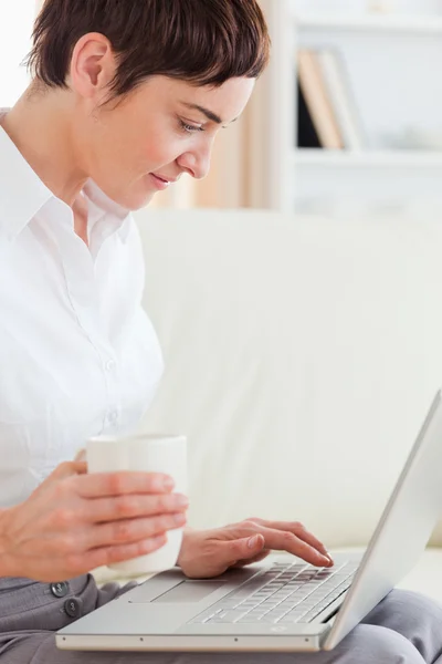 Bir kadın onun kucağına bir dizüstü bilgisayar sahip bir kupa ile yakın çekim — Stok fotoğraf