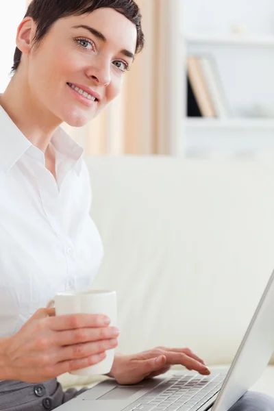 Mulher bonito com uma xícara e um laptop — Fotografia de Stock
