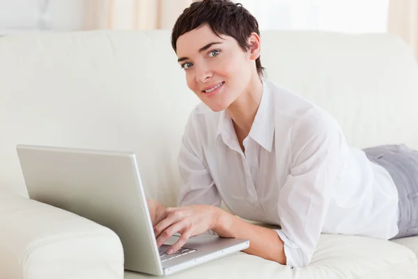 ノート パソコンでソファーに横になっている笑顔の女性 — ストック写真