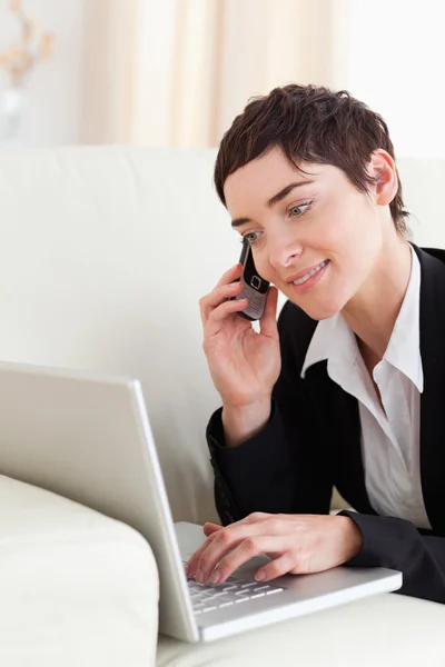 Mujer de negocios acostada en un sofá con un ordenador portátil y un teléfono —  Fotos de Stock