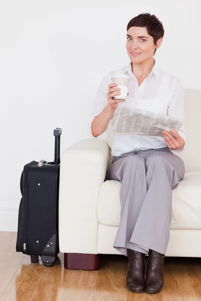 Брюнетка с чемоданом, газетой и чашкой — стоковое фото