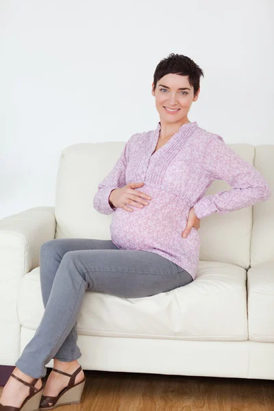ソファーに座って妊娠中の女性の笑みを浮かべてください。 — ストック写真