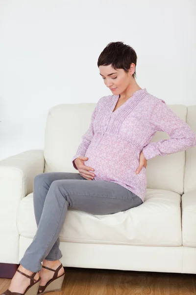 Femme enceinte assise sur un canapé touchant son ventre — Photo