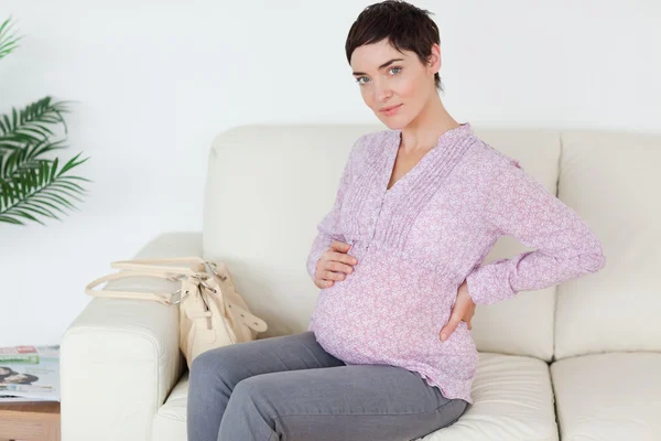Linda mulher grávida sentada em um sofá tocando sua barriga — Fotografia de Stock