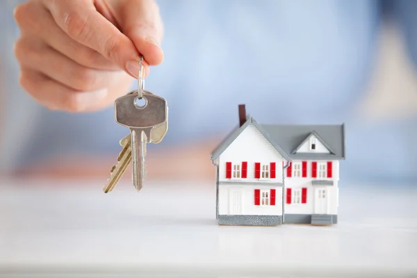 Mulher segurando chaves ao lado de uma casa modelo — Fotografia de Stock