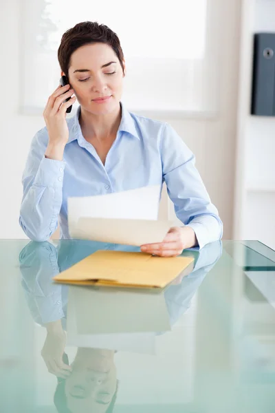 Kobieta siedzi za biurkiem z dokumentów na telefon — Zdjęcie stockowe