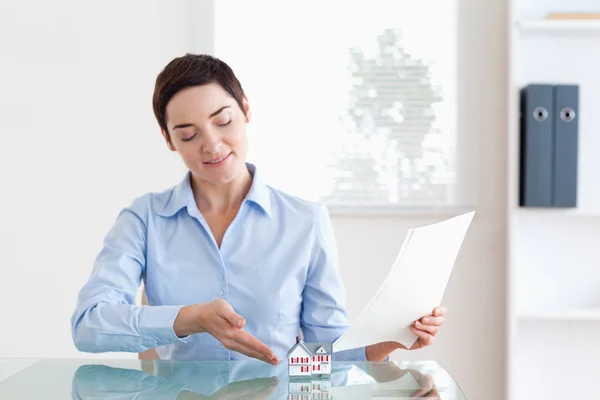 Short-haired Woman holding papers showing a model house — Stock Photo, Image