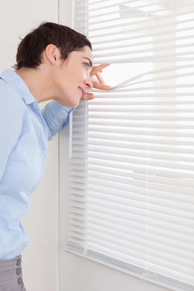 Brunette woman peeking out a window — Stock Photo, Image