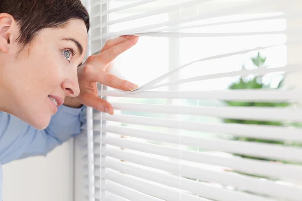 Affascinante donna sbirciando fuori da una finestra — Foto Stock