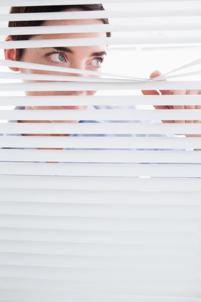 Nyfiken brunett kvinna kikar ut från ett fönster — Stockfoto