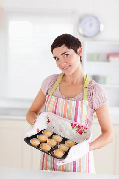 Lächelnde brünette Frau zeigt Muffins, die in die Kamera schauen — Stockfoto