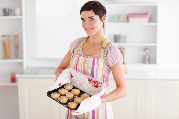 Mulher morena encantadora mostrando muffins olhando para a câmera — Fotografia de Stock