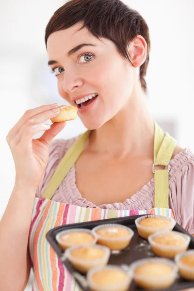 Mulher morena encantadora mostrando muffins enquanto come um — Fotografia de Stock