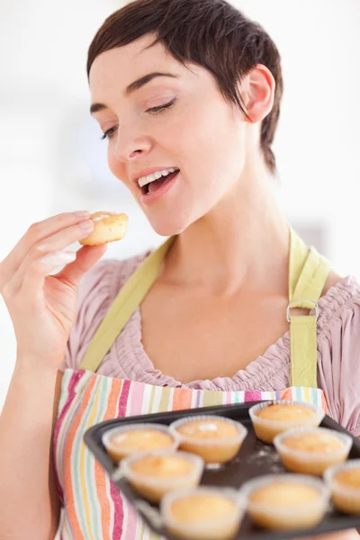 Sorridente donna bruna che mostra muffin mentre ne mangia uno — Foto Stock
