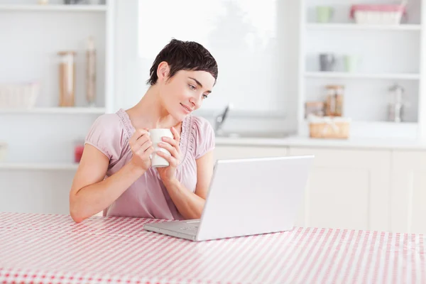 Niedliche Frau arbeitet mit einem Laptop, der eine Tasse hält — Stockfoto
