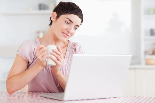 Mujer linda con una taza y un ordenador portátil —  Fotos de Stock