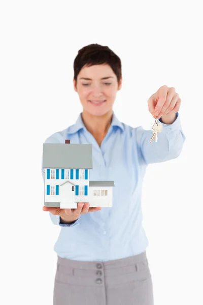 Inmobiliaria mostrando llaves y una casa en miniatura — Foto de Stock