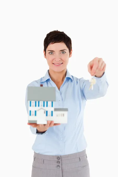 Агент з нерухомості тримає ключі і мініатюрний будинок — стокове фото