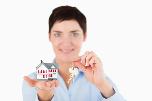 Close up de uma mulher mostrando chaves e uma casa em miniatura — Fotografia de Stock