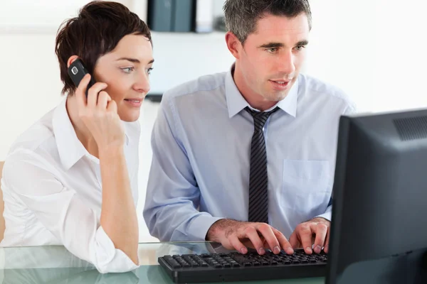 Frau telefoniert, während ihr Kollege einen Computer benutzt — Stockfoto