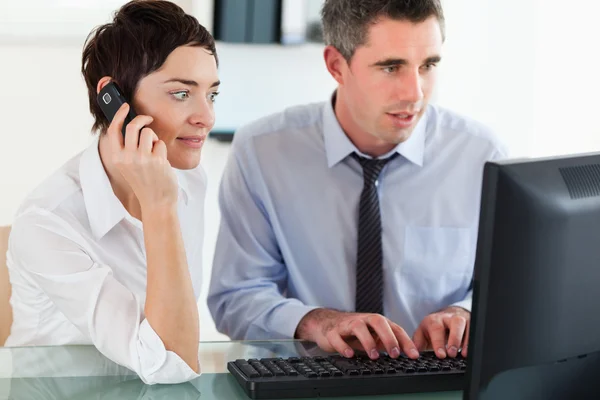 Geschäftsfrau telefoniert, während ihr Kollege einen Rechner benutzt — Stockfoto