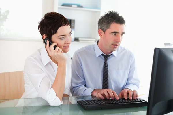 Serious woman telephoning while her colleague is using a compute — Stock Photo, Image