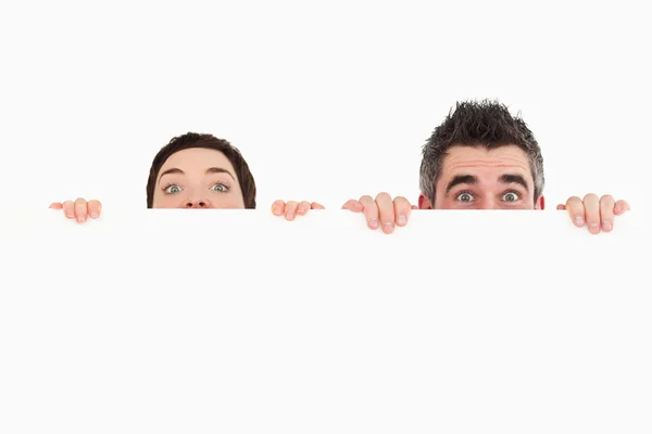Hombre y mujer escondidos detrás de una pizarra blanca con espacio para copiar sp — Foto de Stock