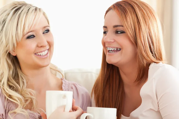 Směje se mladé ženy sedí na pohovce s cups — Stock fotografie