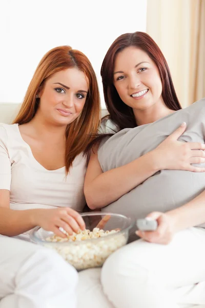 Lächelnde junge Frauen liegen auf einem Sofa und schauen sich einen Film an — Stockfoto