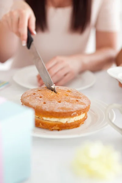 Charming Woman sitting at a table cutting a cake — Stock Photo, Image
