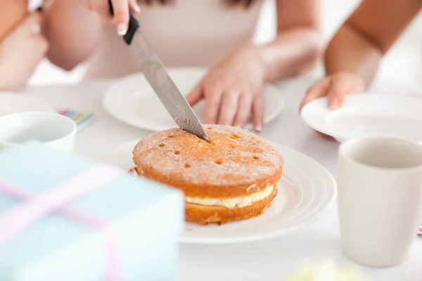 Sevimli kadın pasta keserek bir masada oturuyor — Stok fotoğraf