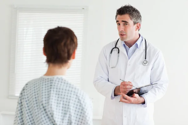 Серйозний лікар розмовляє з жінкою в лікарняній сукні — стокове фото