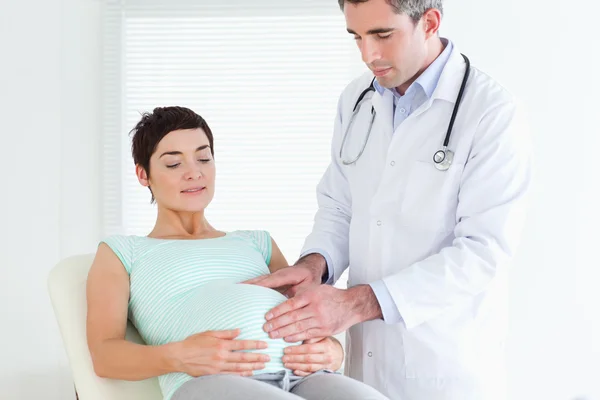 Doutor auscultando a barriga de uma mulher grávida — Fotografia de Stock