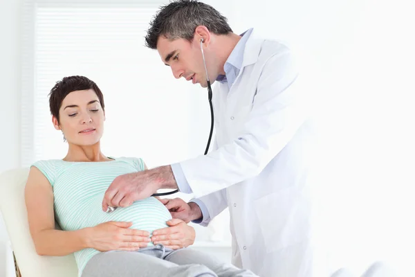 Doctor examinando la barriga de la linda mujer con un estetoscopio —  Fotos de Stock